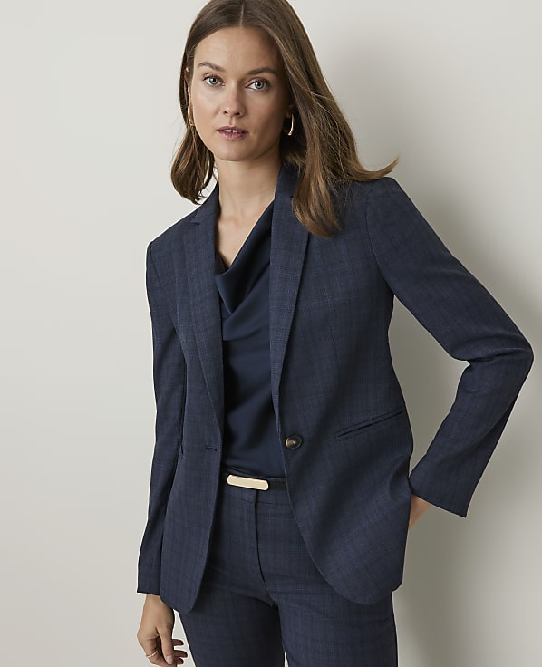 A woman in a navy blue pinstripe suit stands against a plain, light-colored background.