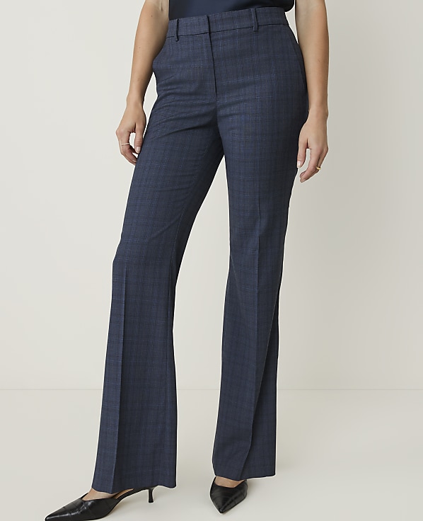 A person wearing blue plaid flared trousers and black pointed-toe heels stands against a plain white background.
