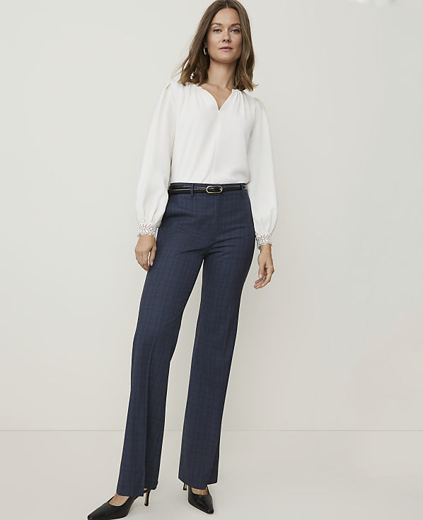 A woman in a white blouse and dark blue pants stands against a plain white background.