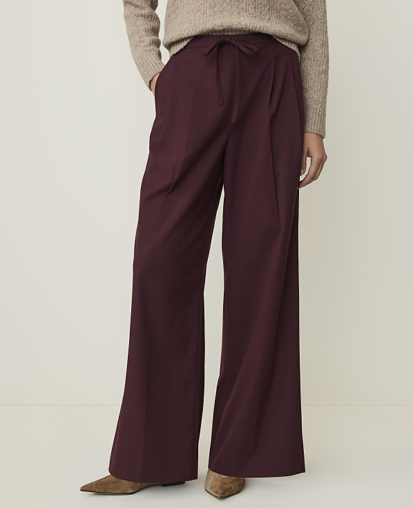 A person in a beige sweater and burgundy wide-leg pants stands against a plain white background.