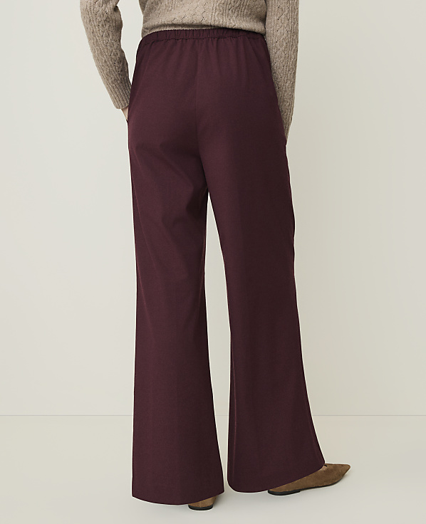 A person wearing burgundy flared pants and a beige sweater stands against a plain, light-colored background.