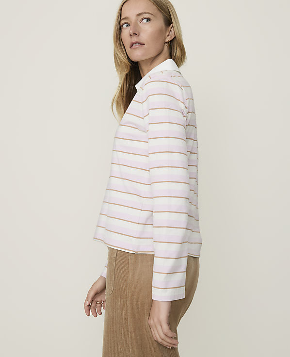 A woman in a striped shirt and corduroy skirt stands against a plain, light background.