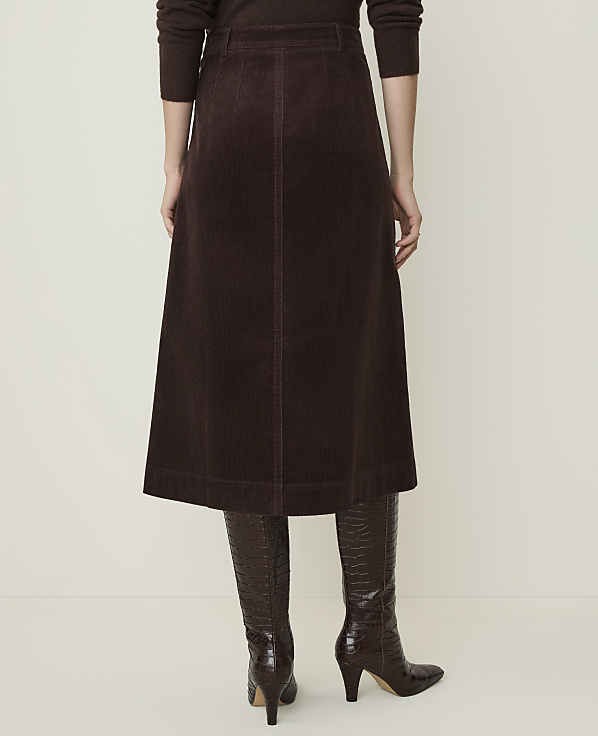 A person wearing a brown corduroy skirt and matching boots stands against a plain, light-colored background.