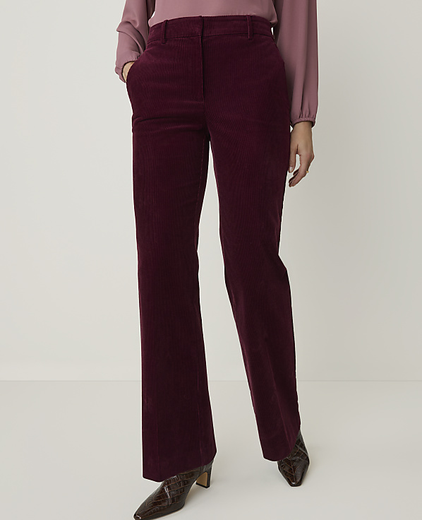 A person stands in burgundy corduroy pants and a pink blouse against a plain white background.