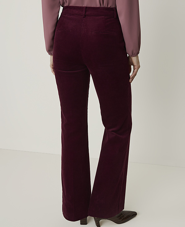 A person wearing burgundy corduroy flared pants and a mauve blouse stands against a plain white background.