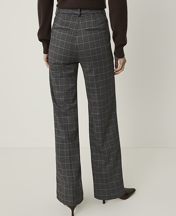 A person wearing plaid wide-leg pants and a brown sweater stands against a plain white background.