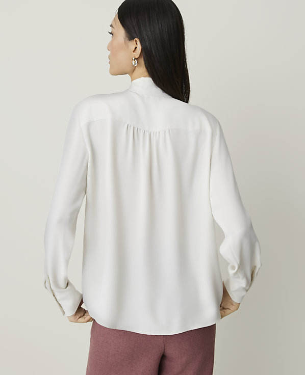 A woman in a white blouse and pink pants stands against a plain background.