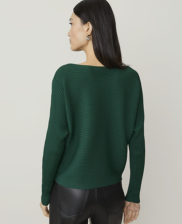 A woman in a green ribbed sweater and black leather pants stands against a plain, light gray background.