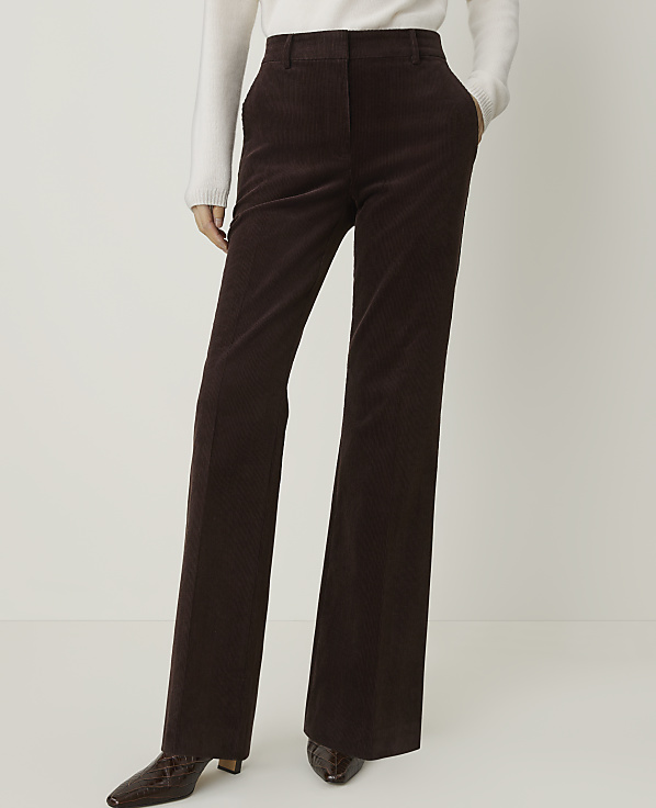 A person in brown corduroy pants and a white sweater stands against a plain white background.