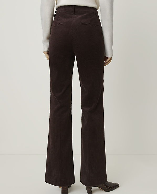 A person wearing brown corduroy pants and a white sweater stands against a plain white background.