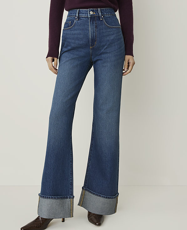 A person wearing high-waisted, flared jeans with large cuffs stands against a plain white background.