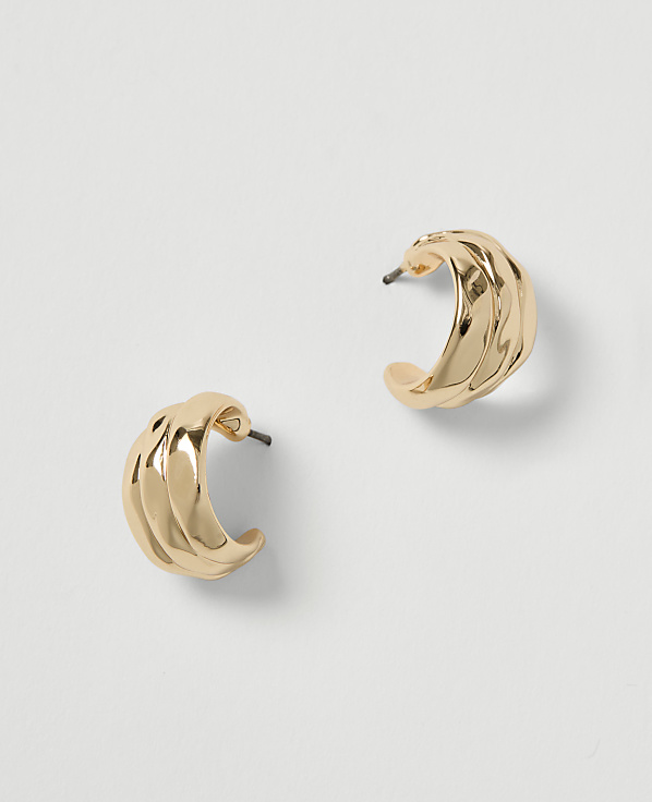 A pair of textured gold hoop earrings rests on a plain white background.
