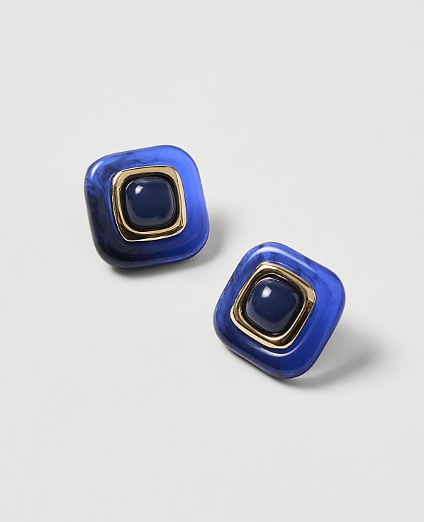 Two square blue earrings with gold trim and a dark blue center stone rest on a light gray background.