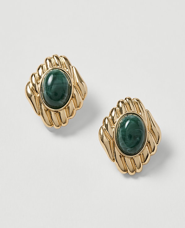 A pair of gold earrings with oval green stones are displayed against a plain white background.
