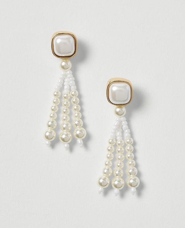 A pair of elegant pearl drop earrings with gold-toned square tops hang against a plain white background.