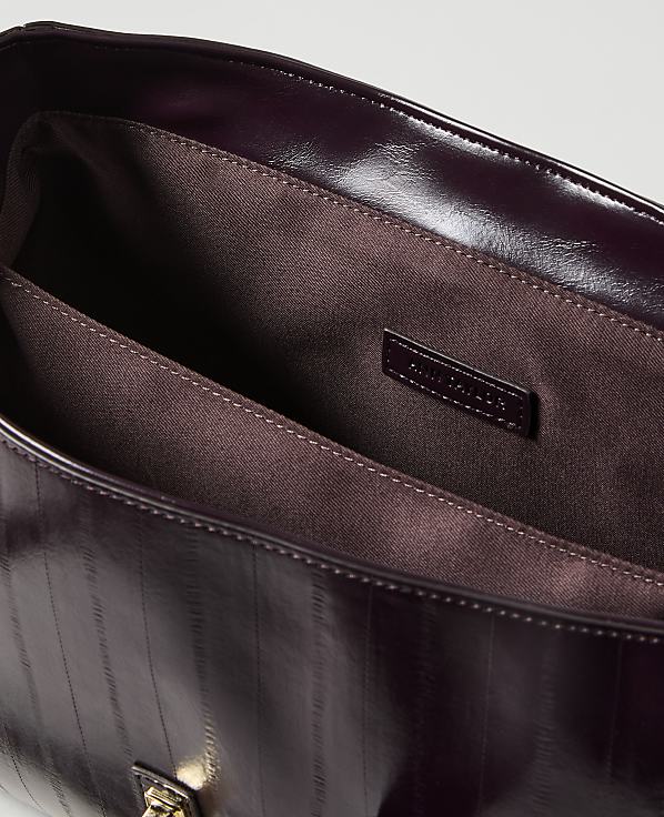 A glossy, dark purple handbag with vertical stitching is open in the foreground, revealing its brown fabric lining and a small brand tag, against a plain, light background.