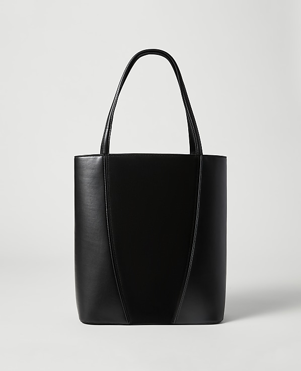 A sleek black leather tote bag with a V-shaped seam stands against a plain, light gray background.