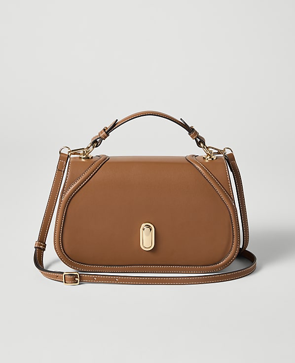 A brown leather handbag with a gold clasp sits in the foreground against a plain, light gray background.