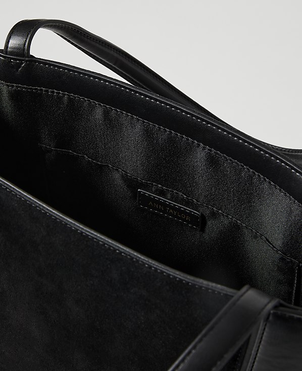 A black leather tote bag with a branded label is shown against a plain white background.