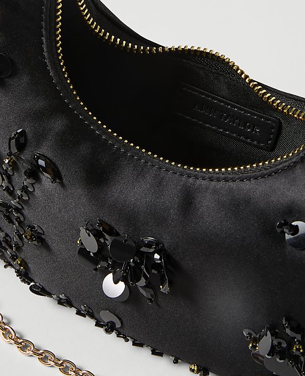 A black satin handbag adorned with sequins and beads is shown in the foreground, with a glimpse of its interior and a gold chain strap, against a plain white background.