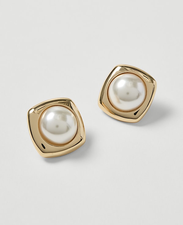 A pair of gold-toned square earrings with pearl inlays rests on a plain white background.