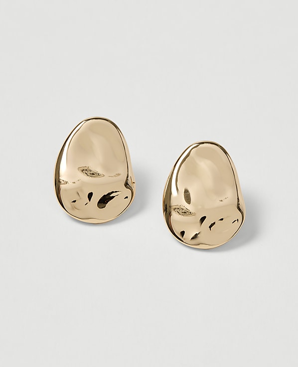 Two polished gold earrings with an organic, pebble-like shape rest on a plain, light gray background.
