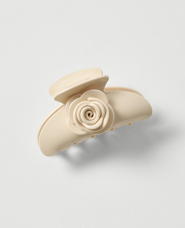 A cream-colored claw clip with a rose embellishment rests on a plain, light gray background.