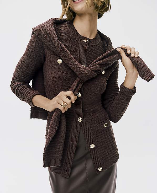 A woman in a brown ribbed cardigan and skirt poses against a plain white background, with a matching scarf draped over her shoulders.