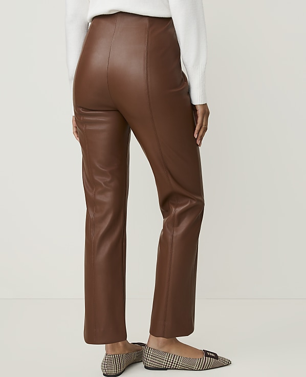 A person wearing brown faux leather pants and plaid flats stands against a plain white background.