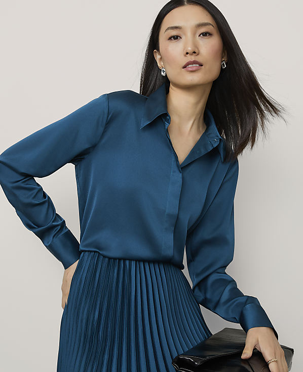 A woman in a teal satin blouse and pleated skirt poses against a plain white background.
