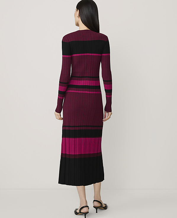 A woman in a long-sleeved, striped knit dress stands against a plain, light-colored background.