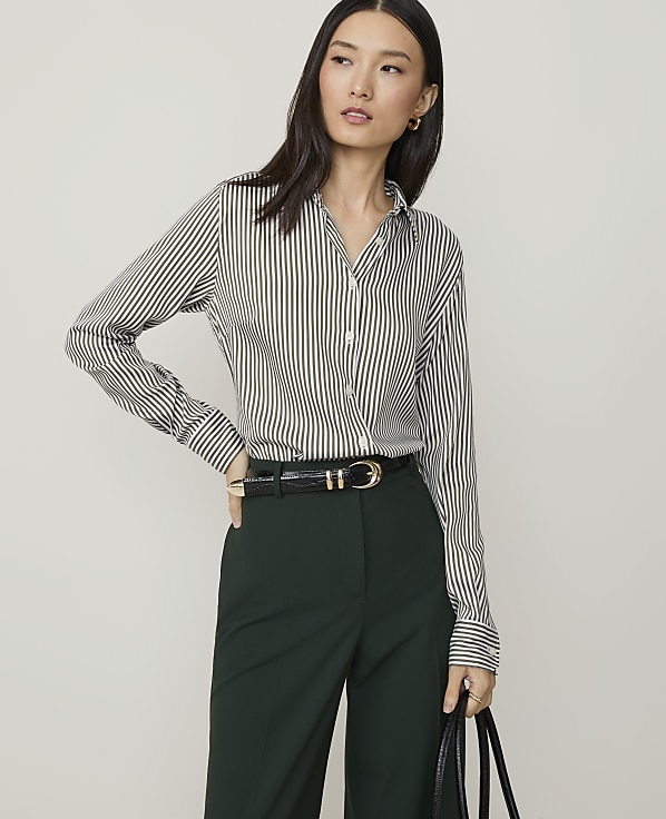 A woman in a striped shirt and brown suede skirt stands against a plain white background.