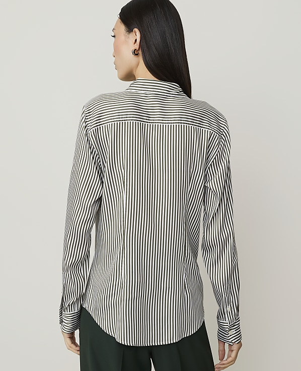 A woman in a striped shirt and brown skirt stands against a plain white background.