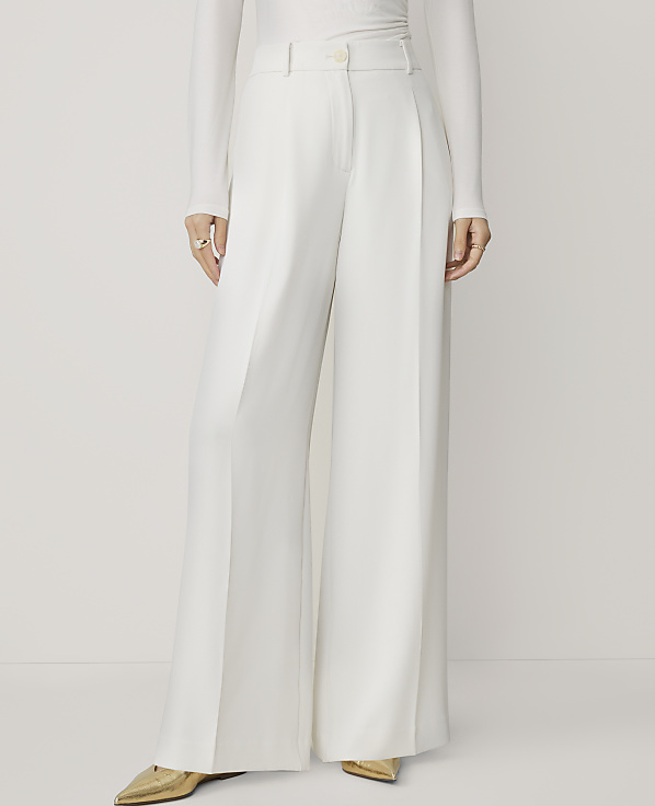 A person wearing white wide-leg pants and gold pointed-toe shoes stands against a plain white background.