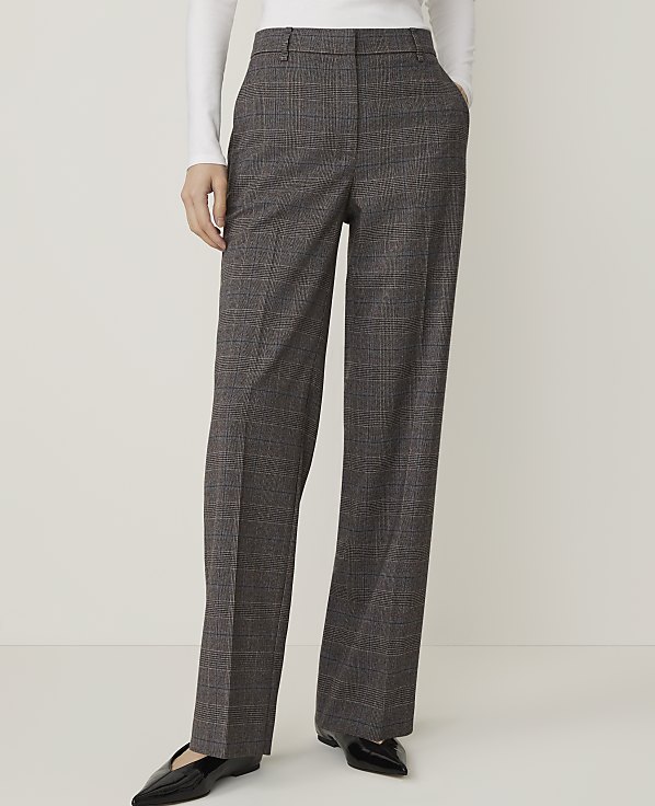 A person stands with hands in the pockets of their grey plaid wide-leg trousers against a plain white background.