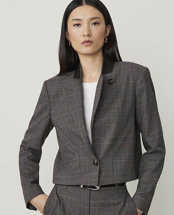 A woman in a plaid jacket and pants stands against a plain, light gray background.