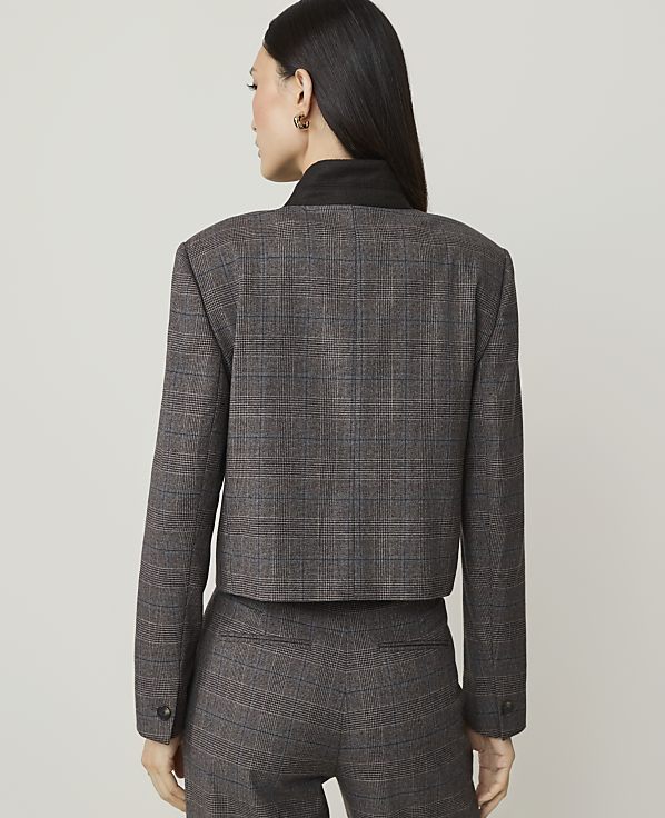 A woman in a plaid suit stands against a plain, light-colored background.