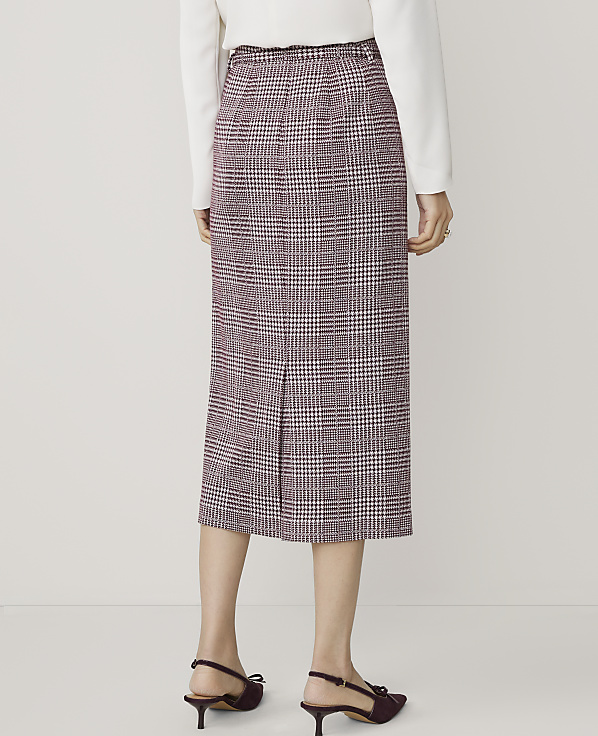 A person wearing a plaid skirt and heels stands against a plain white background.