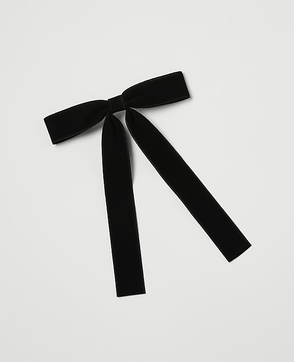 A black velvet bow with long, trailing ribbons lies on a plain white background.