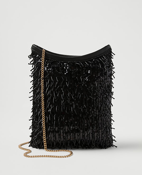 A black sequined fringe bag with a gold chain strap rests against a plain white background.