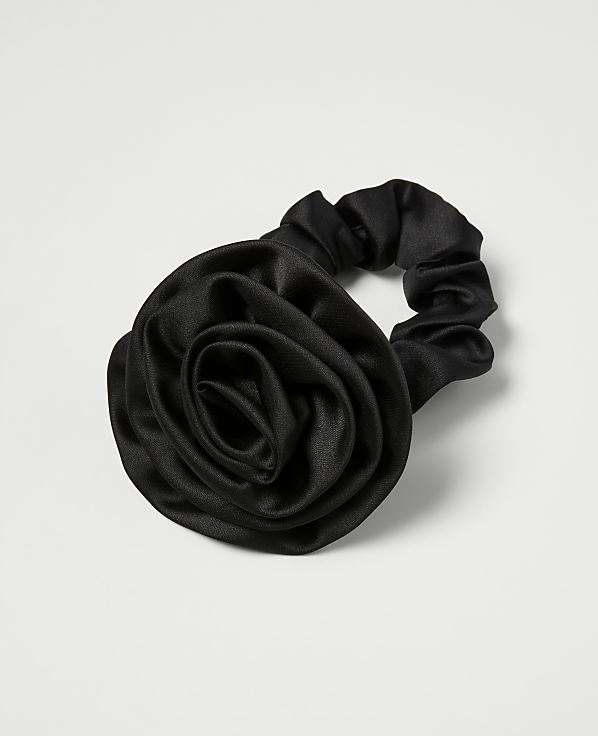 A black satin scrunchie with a rose embellishment rests on a plain white background.