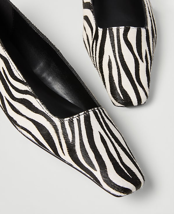 A pair of zebra-print flats with square toes are arranged on a plain white background.