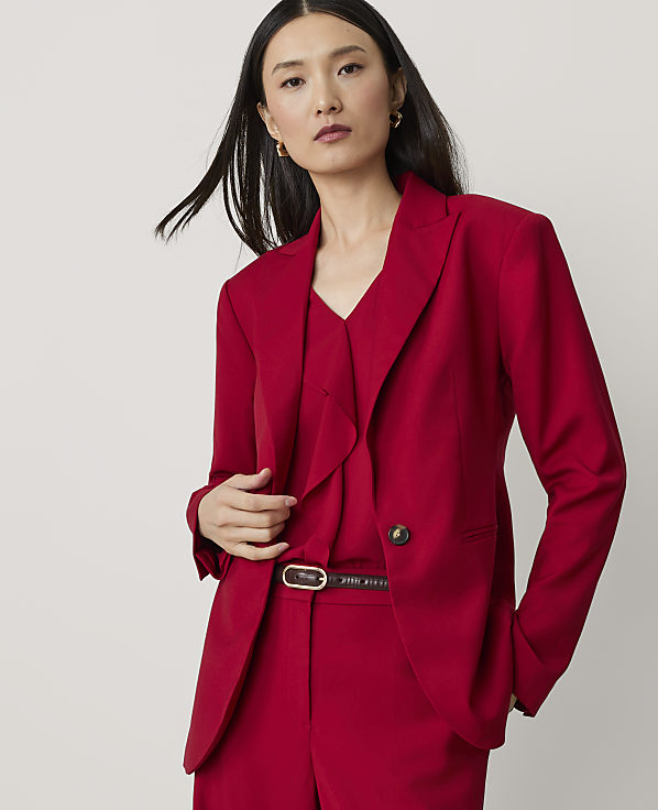A woman in a red blazer and pants stands against a plain, light gray background.