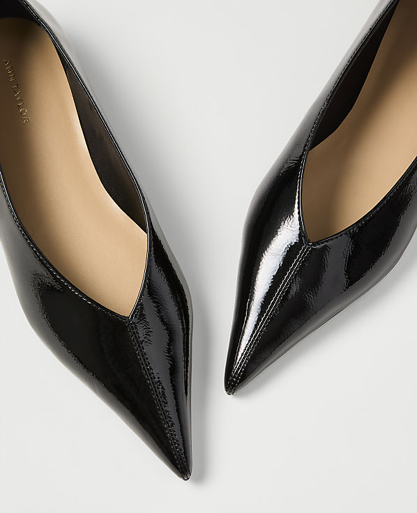 Two glossy black pointed-toe heels are angled towards each other against a plain white background.
