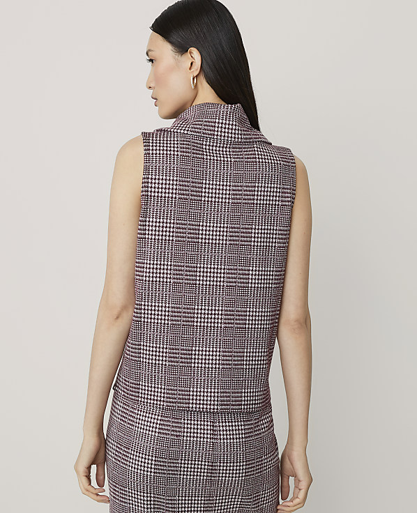 A woman in a plaid vest and skirt stands against a plain background.
