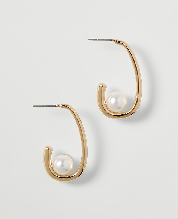 A pair of gold hoop earrings, each with a single pearl nestled within its curve, are displayed against a plain, light gray background.