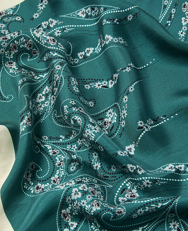 A teal fabric with a white floral paisley pattern is draped over a light-colored surface.