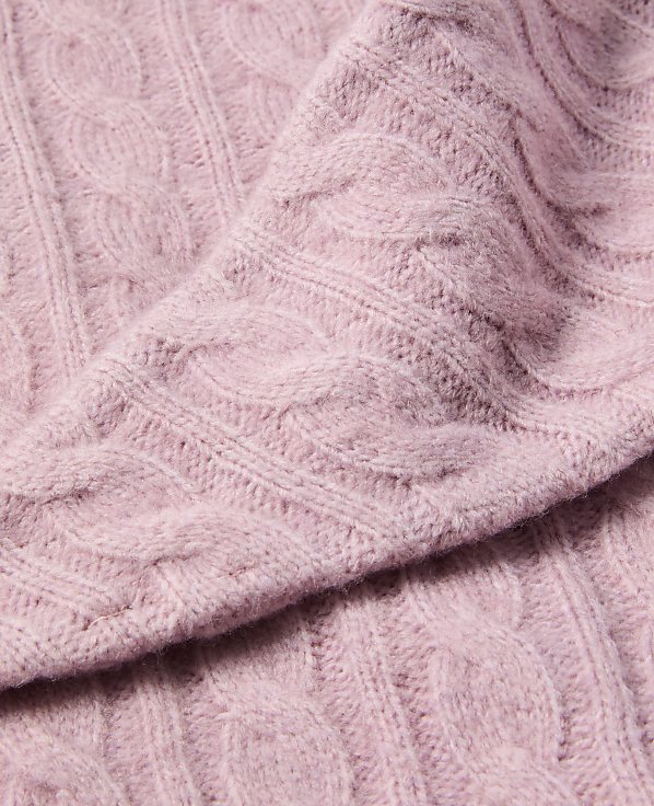 A close-up of a soft, pink cable-knit sweater fills the frame, with the textured fabric creating a cozy and inviting foreground against a subtly blurred background.