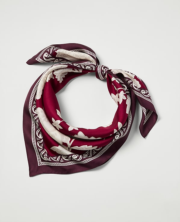 A burgundy and cream patterned silk scarf is tied in a knot against a plain white background.