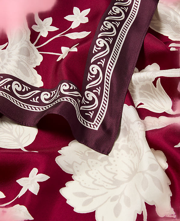 A burgundy silk scarf with a white floral pattern is draped over a matching fabric, with a decorative border visible in the foreground.